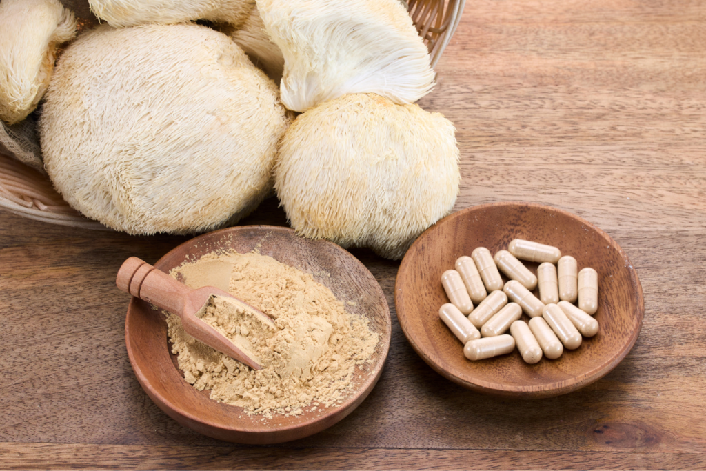 Vetrestudio no Canva Pro Cogumelos Juba de Leão e suplementos naturais em pó e em cápsulas, dispostos em tigelas de madeira em uma superfície de madeira rústica.